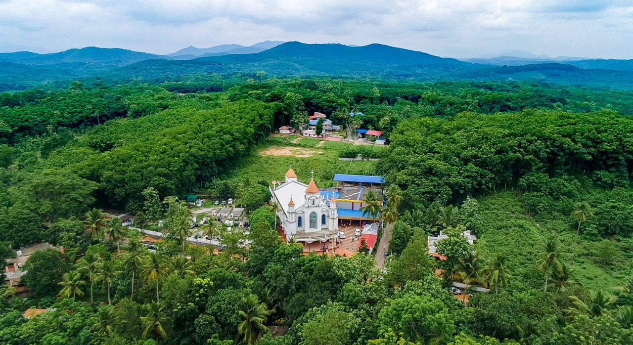 Aerial view of St. Mary's Orthodox Syrian Church among the green hills of Alencherry